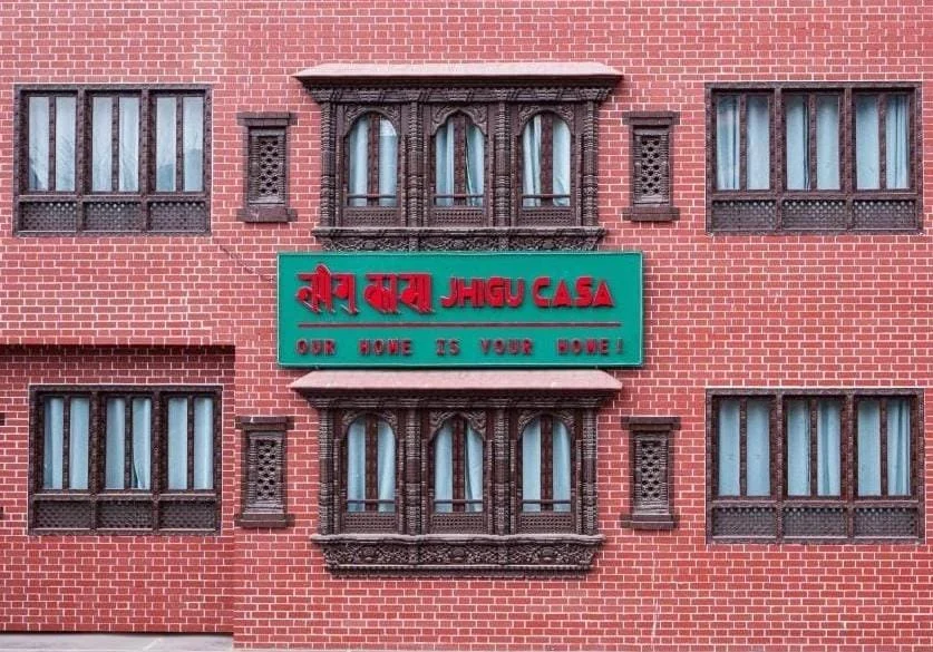 The red-brick Newari facade of Jhigu Casa in Kirtipur, with carved wooden windows and the house sign.